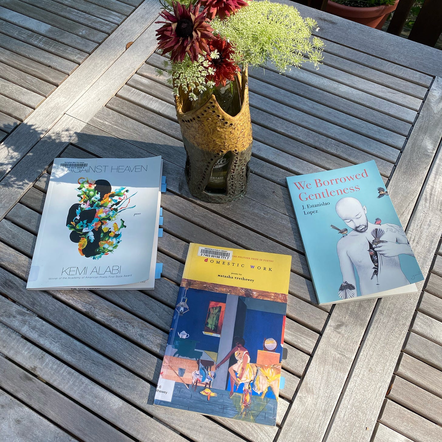 Against Heaven, Domestic Work, and We Borrowed Gentleness lie on a sunny porch table next to a vase of Queen Anne’s Lace and red rudbeckia.