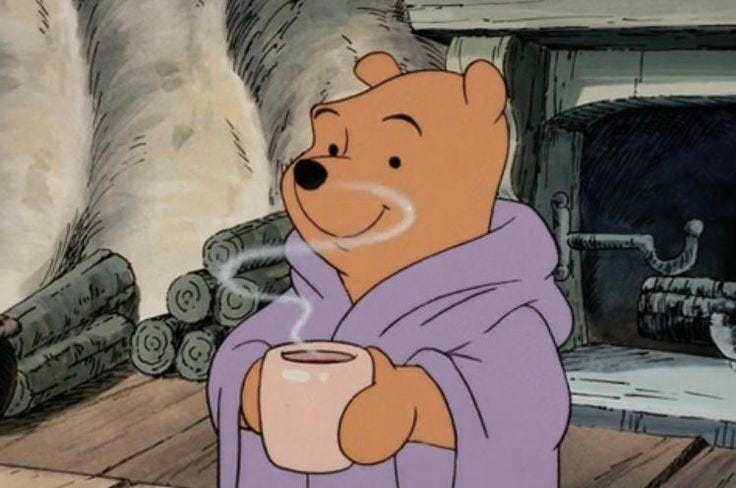 This may contain: winnie the pooh is holding a coffee cup in front of a fireplace with logs