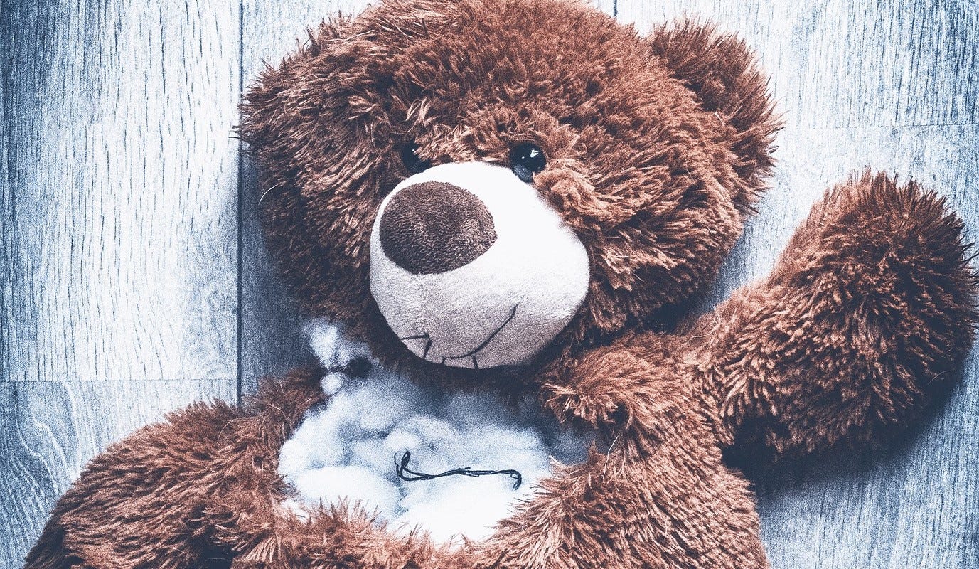 A teddy bear, its neck torn open and stuffing exposed.
