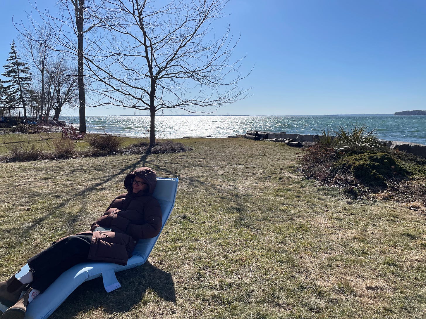 a white woman bundled up in a reclining chair by the water
