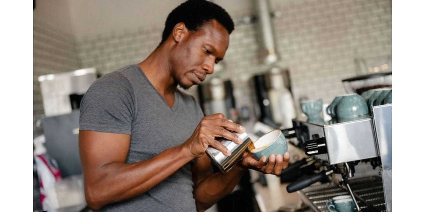 A man focuses on pouring steamed milk into a coffee mug.