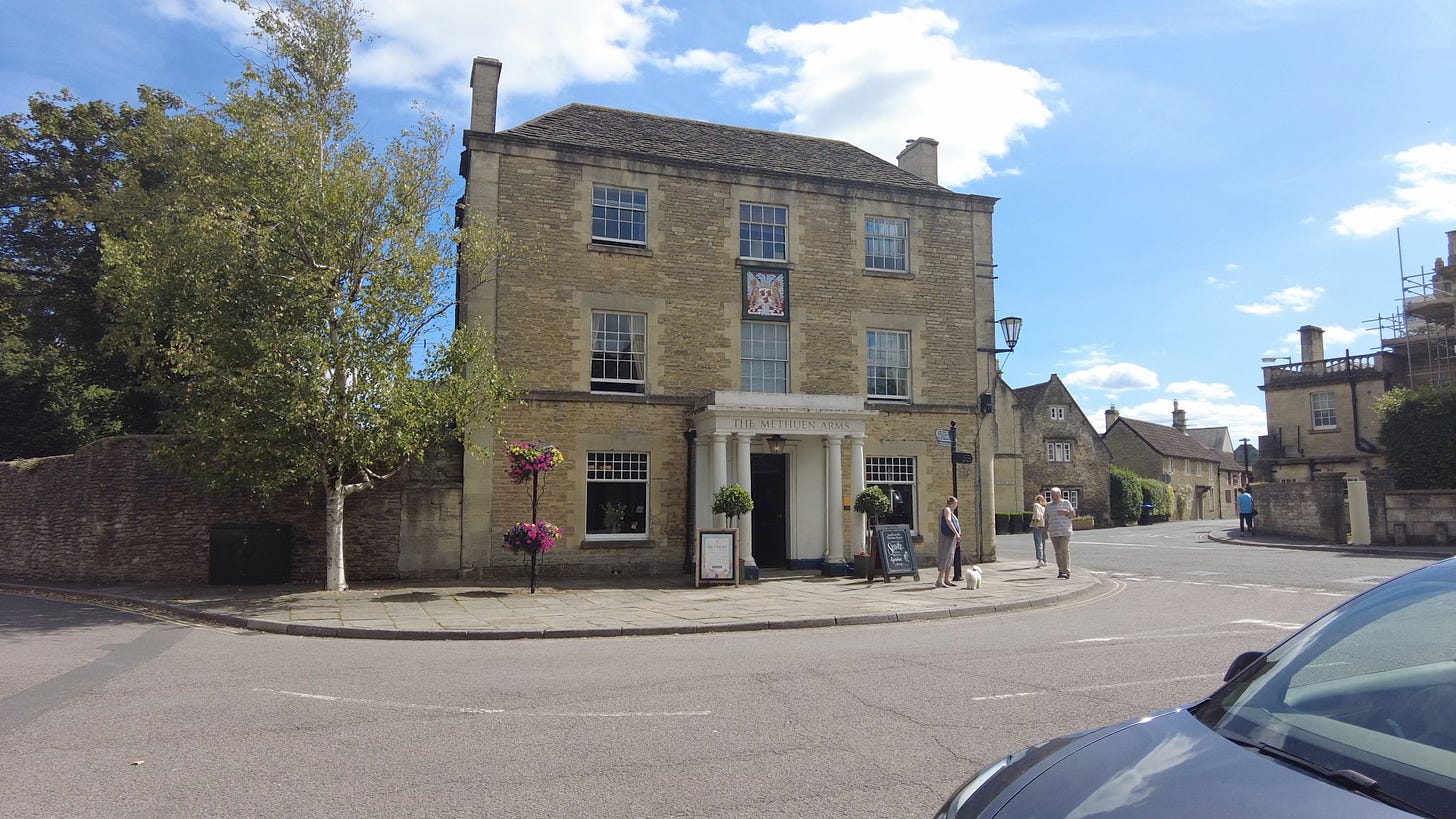 The Methuen Arms. 2 High Street, Corsham, Wiltshire. Some people one with a dog are standing on the footpath to one side of the entrance. Image: Roland's Travels