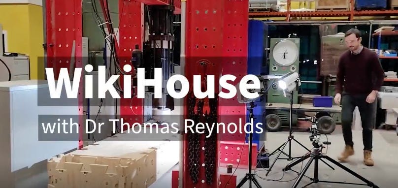 Still from a video, it reads WikiHouse with Dr Thomas Reynolds - Thomas can be seen in the background standing in a lab. He is about to test a WikiHouse block