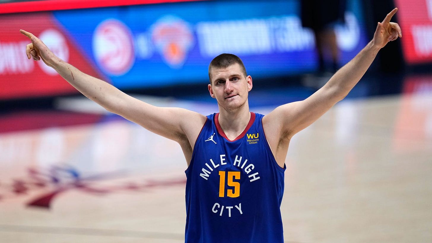 Nikola Jokic raises both arms in salute during a basketball game