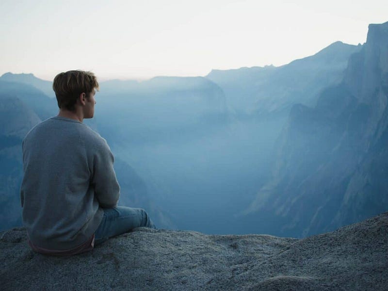 Person sitting on the edge of mountain lookout point, looking into the distance