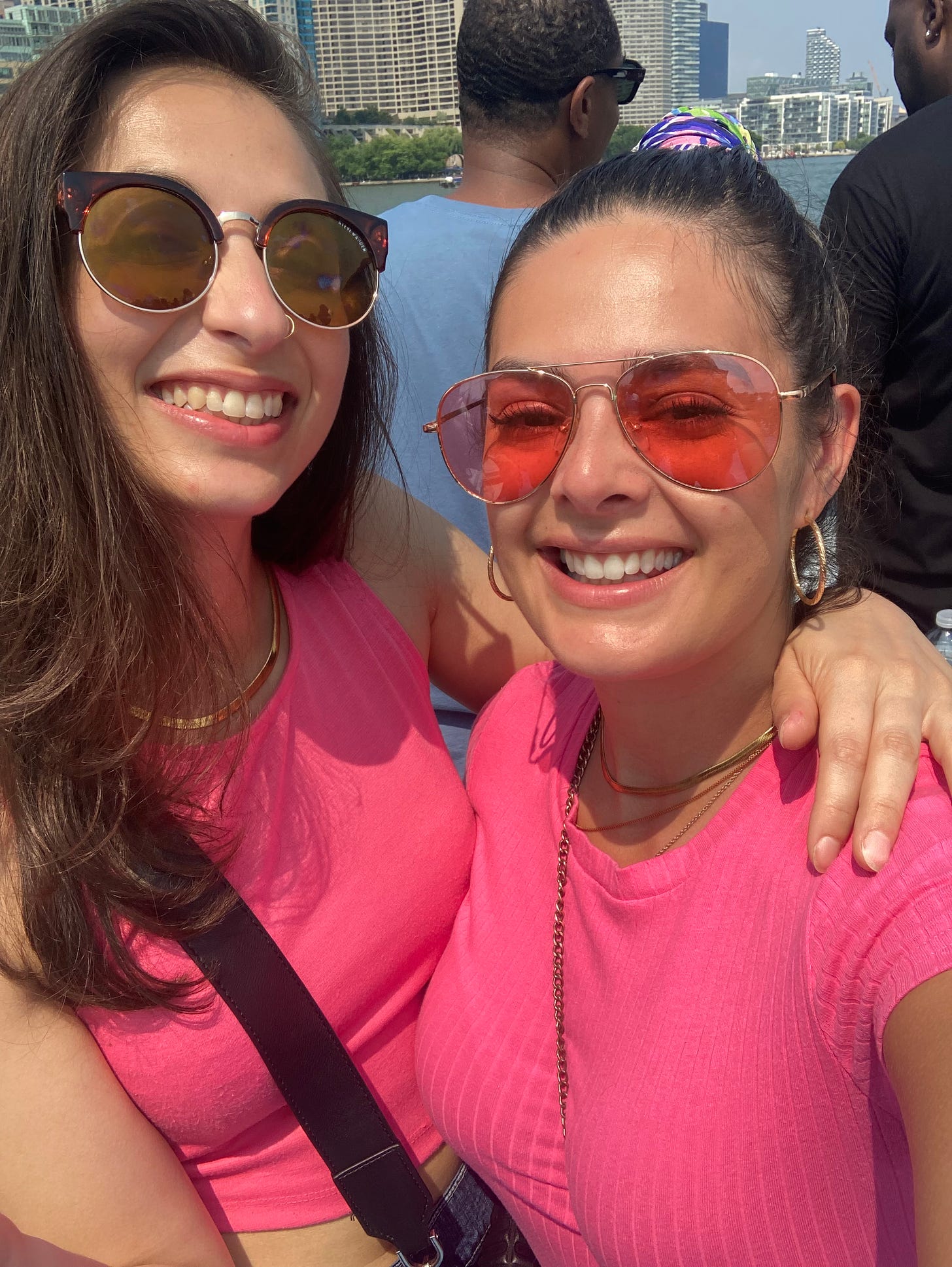 Two girls wearing sunglasses and pink shirts on a boat.