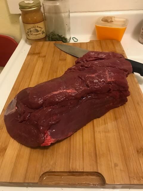 A rectangular brick of elk meat on a cutting board with a knife.