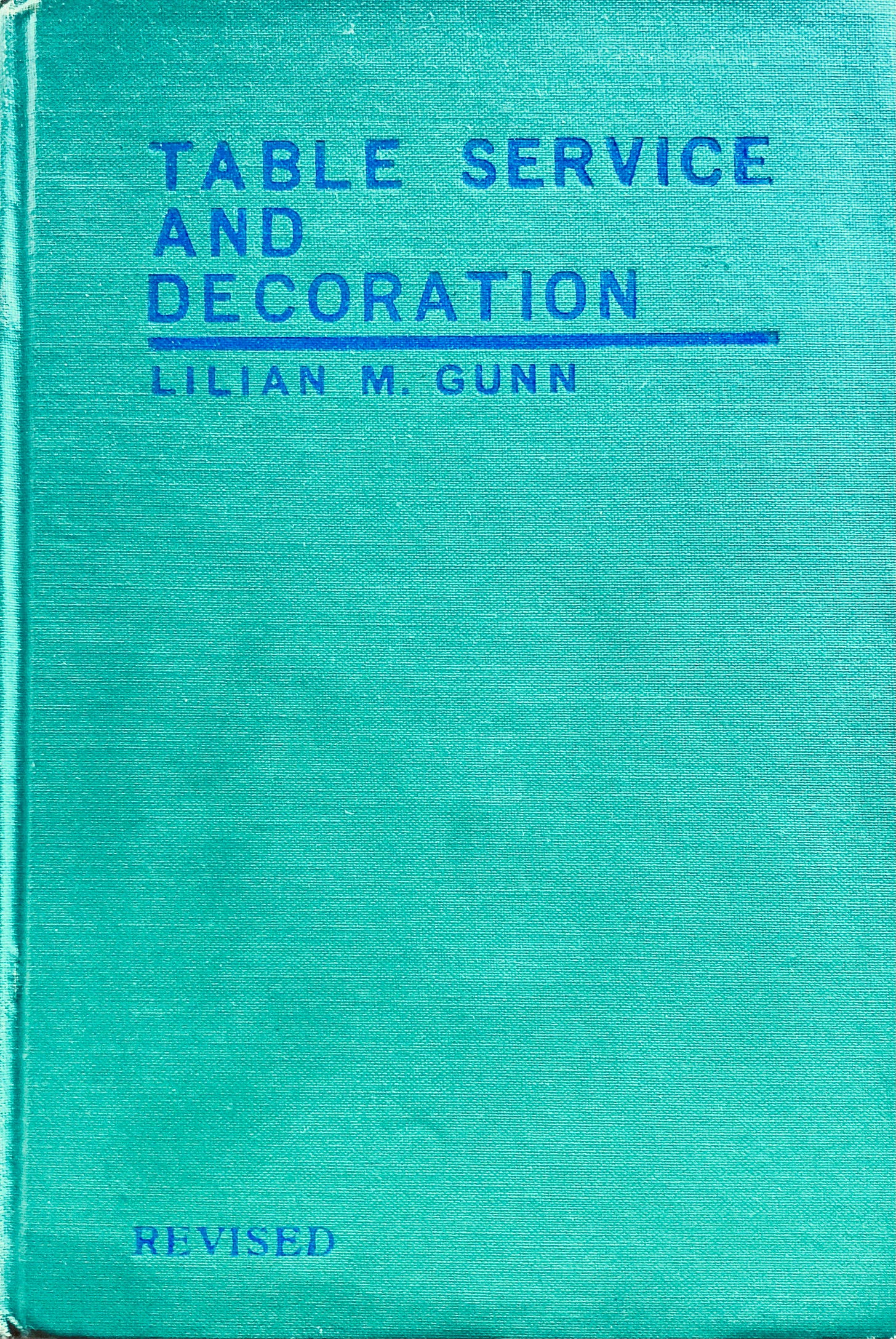 Tealy green cloth bound cover to an old book with Blue debossed font that reads Table Service and Decoration Lilian M. Gunn Revised.