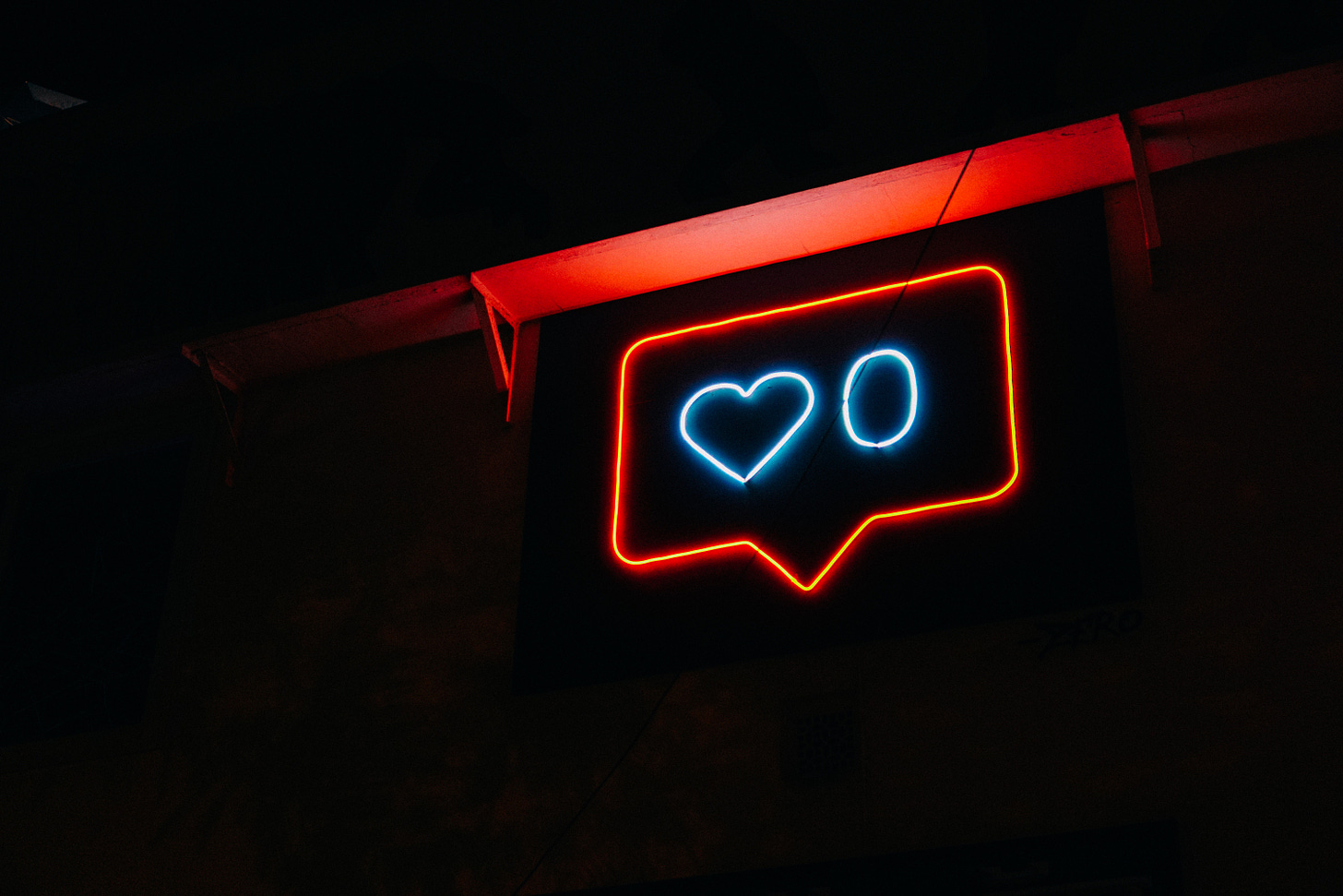 A Red and white neon sign that is a :like: heart with the number on a dark wall