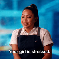 Gif of brown skinned woman with black hair and a high, long pony tail saying “Your girl is stressed,” in a talking head clip from a reality show. She sits in the foreground in a white button up short sleeve shirt and black apron. The background is a blurry blue image. 