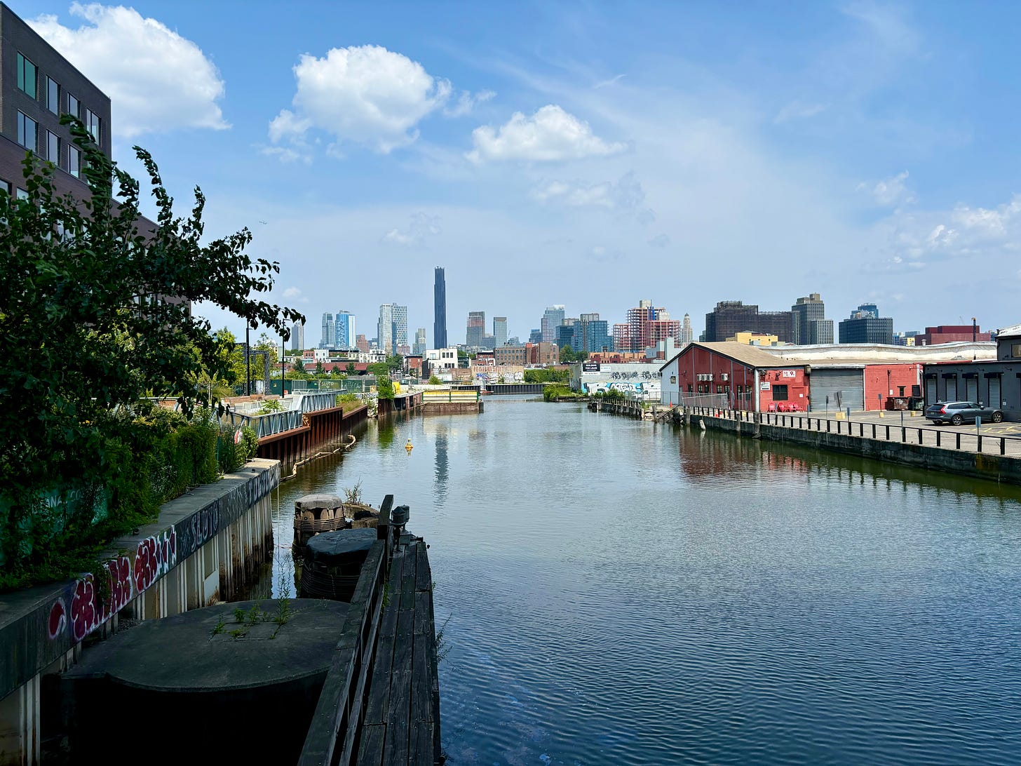 Gowanus Canal under a blue sky. The water reflects the skyscrapers in the distance.