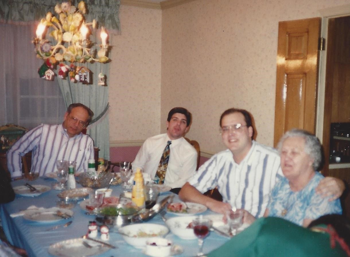 Family gathered around a holiday dinner table. A young adult grandson has his arm around grandmom's shoulder