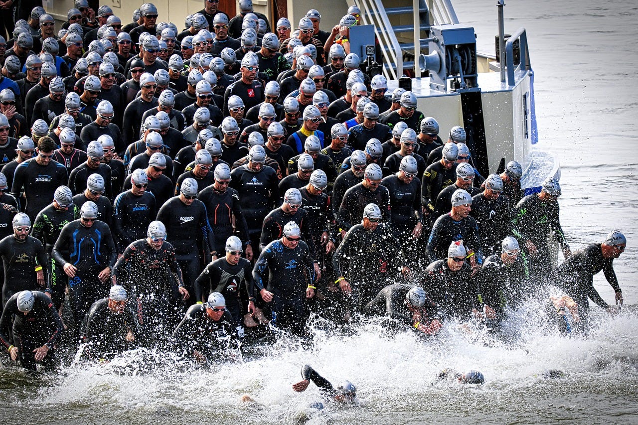 Men  in black triathlon suits line up at start of race. The front jumps up.