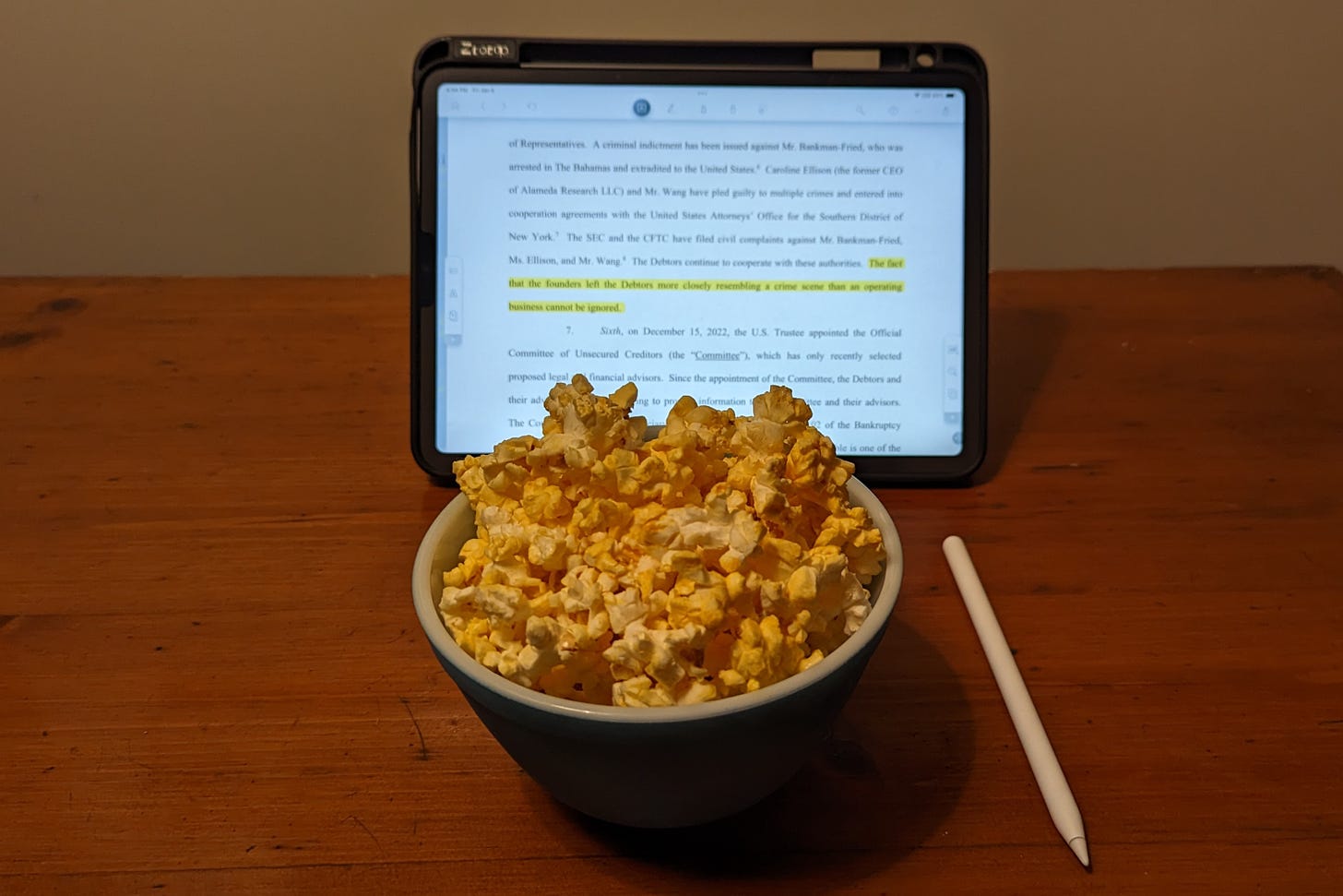 A bowl of popcorn placed in front of an iPad, which displays a PDF of a legal filing with some highlighted text.