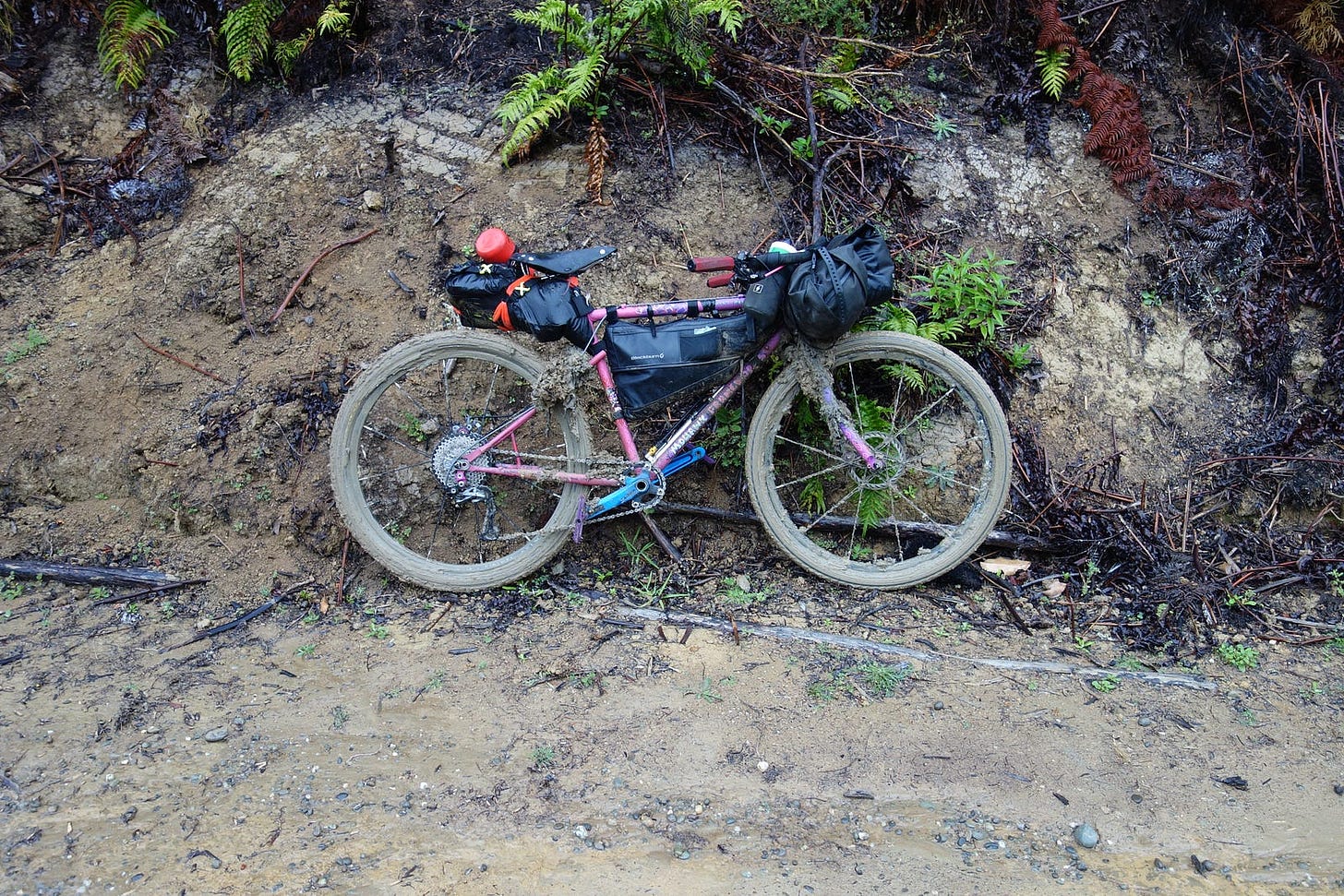 Sarah’s bike is leant against a muddy bank. The wheels are completely clogged with thick mud.