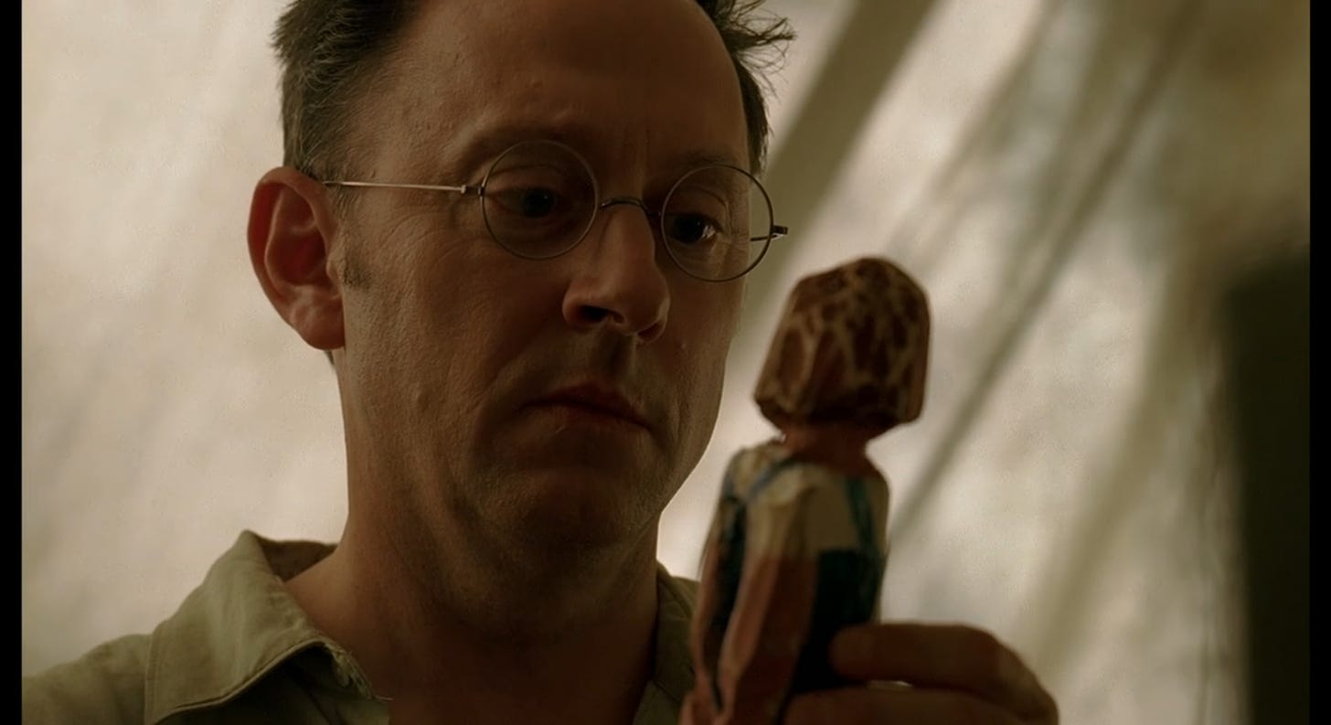 Ben Linus looks at a wooden statue.