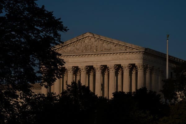 The front of the U.S. Supreme Court building surrounded by trees and in low light.