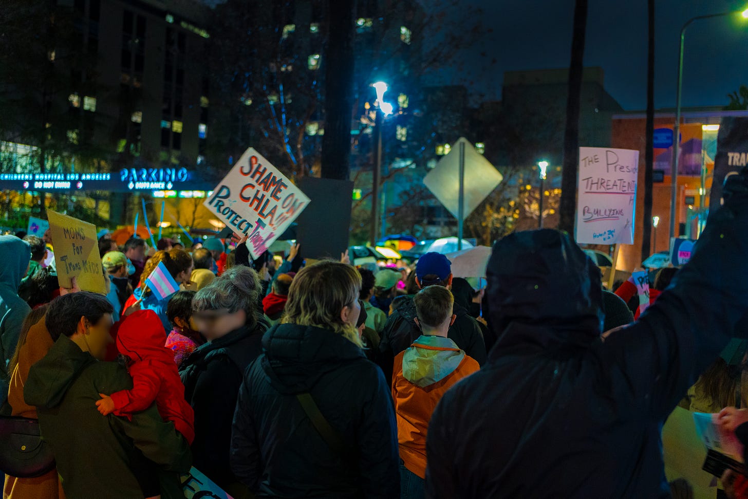 A close up view of the protest from behind, with a sizable crowd of people holding signs facing the street