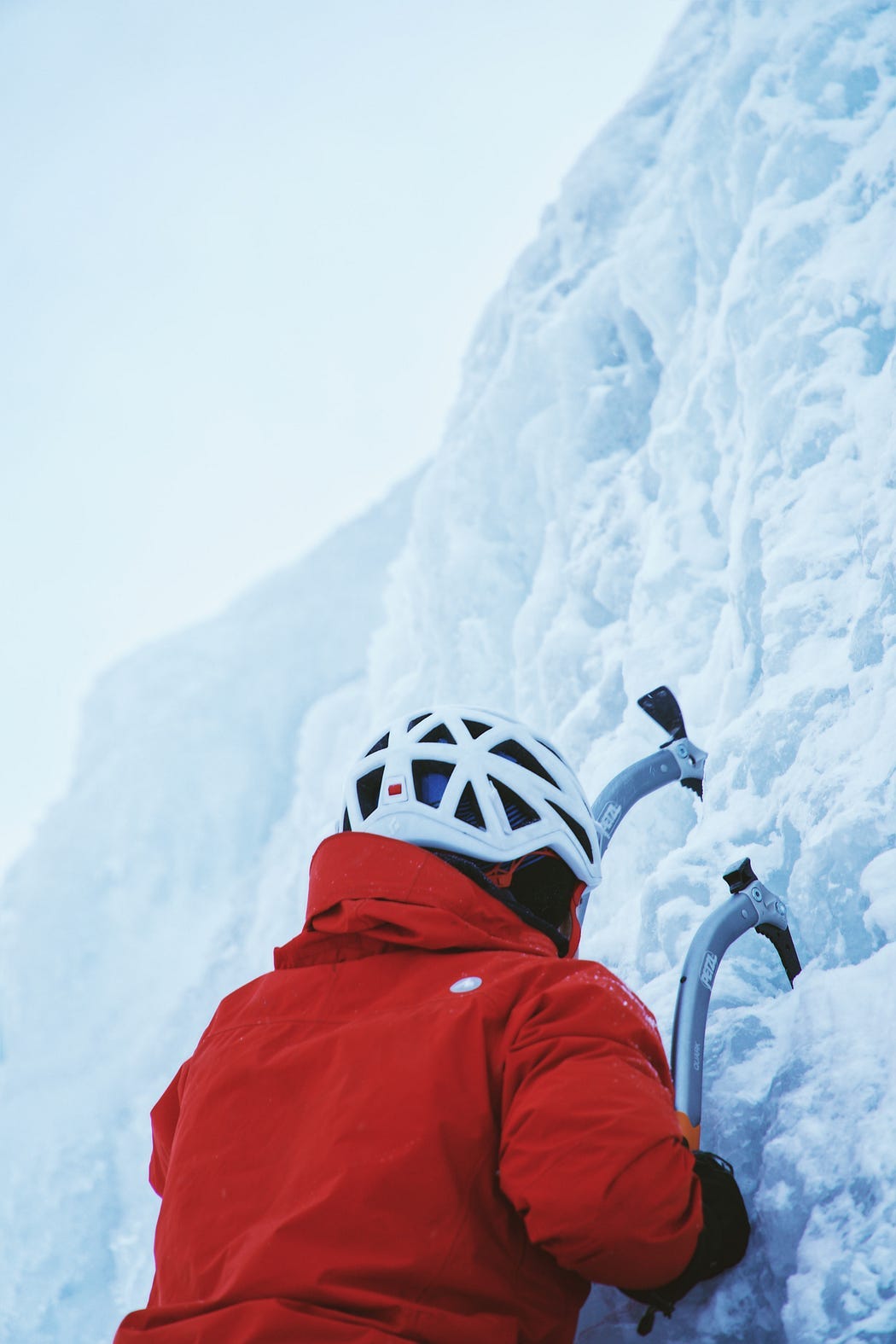 Person in red jacket climbing almost vertical ice wall