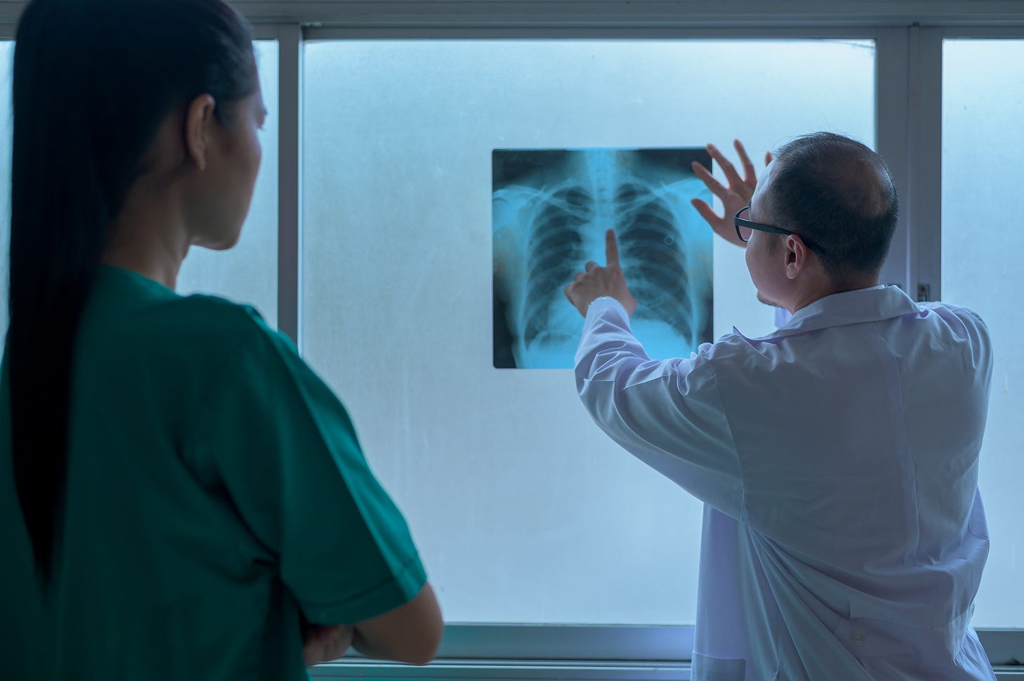 A doctor shows a patient a chest x-ray and points approximately to where the heart is located.