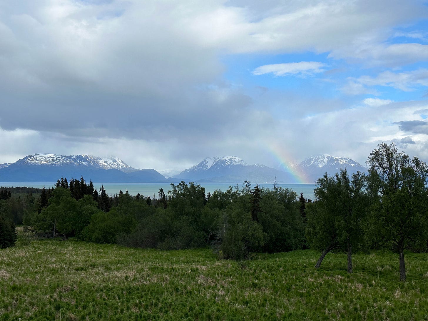 Mountain scene with rainbow coming from cloudy sky.