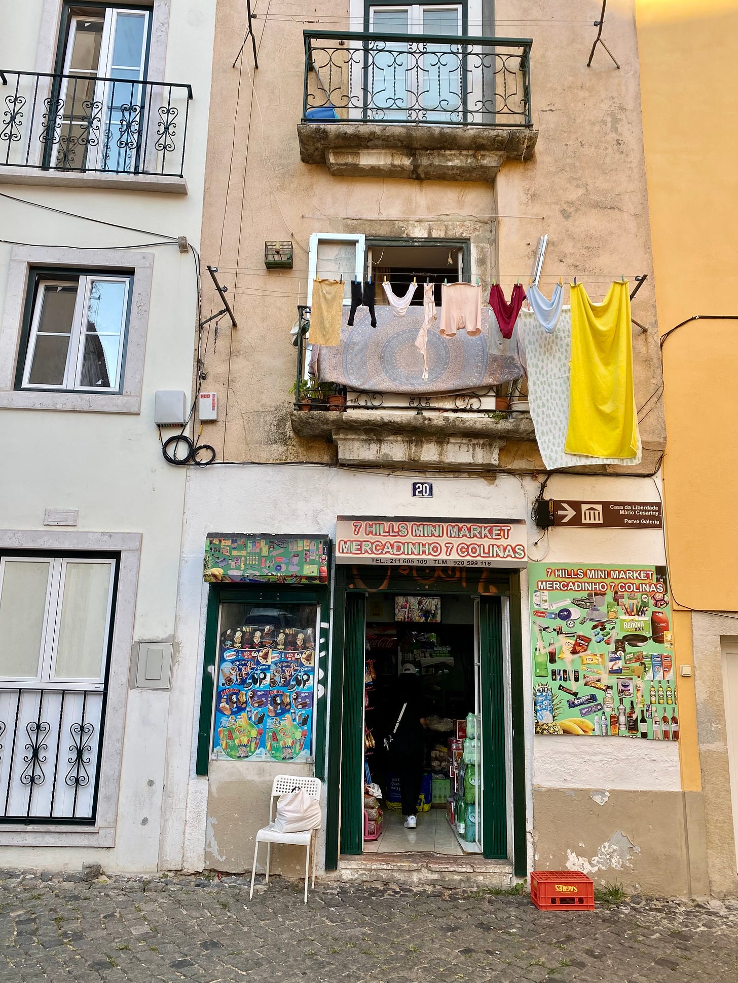 A building in Lisbon with washing hanging from the first floor balcony and a shop door below