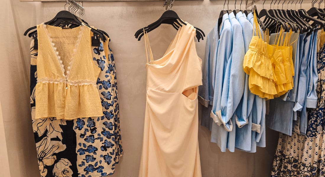 A stone clothing store wall with yellow, blue, and floral patterned garments hanging from the rail