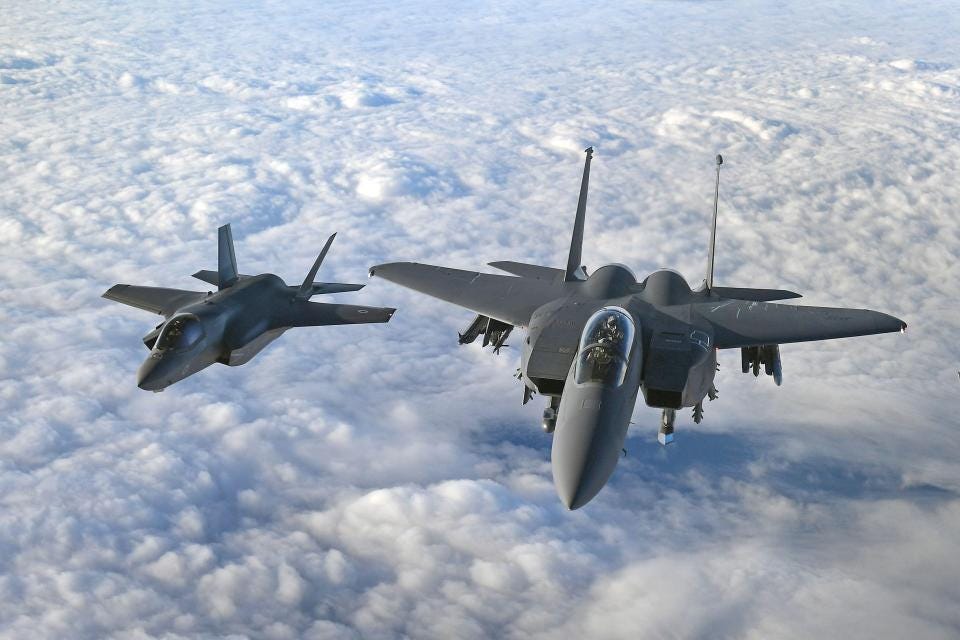 RAF F-35B Lightning and US Air Force F-15 Strike Eagle fighter jets flying above clouds.