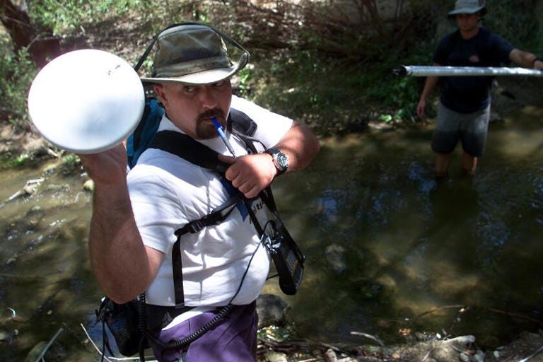 Mark Abramson reaches for the antenna of his global satellite positioning system after taking measurements at a small pool along Las Virgenes Creek in August 2000. ((George Wilhelm / Los Angeles Times))