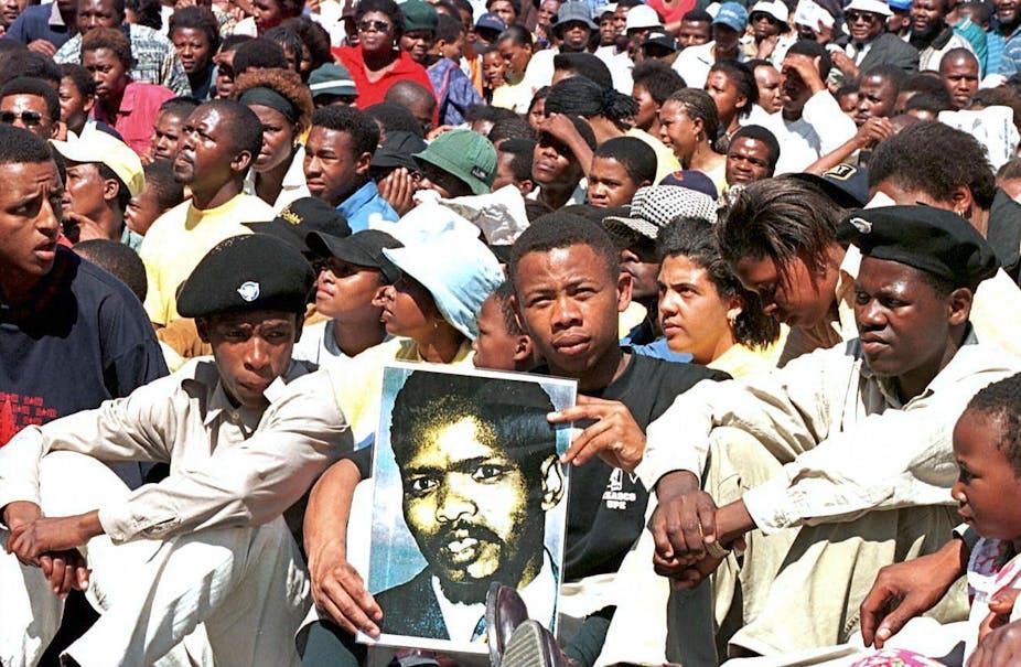 Crowd of seated people, with one holding up a poster of a man's face