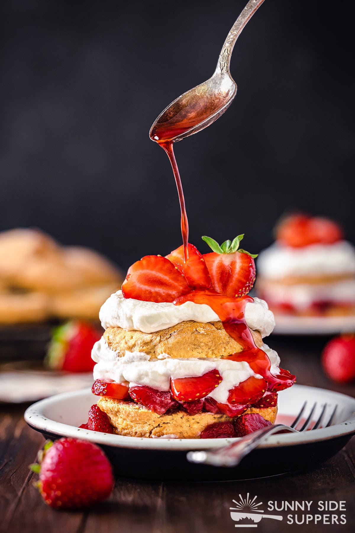 A spoon drizzling sauce onto strawberry shortcake.