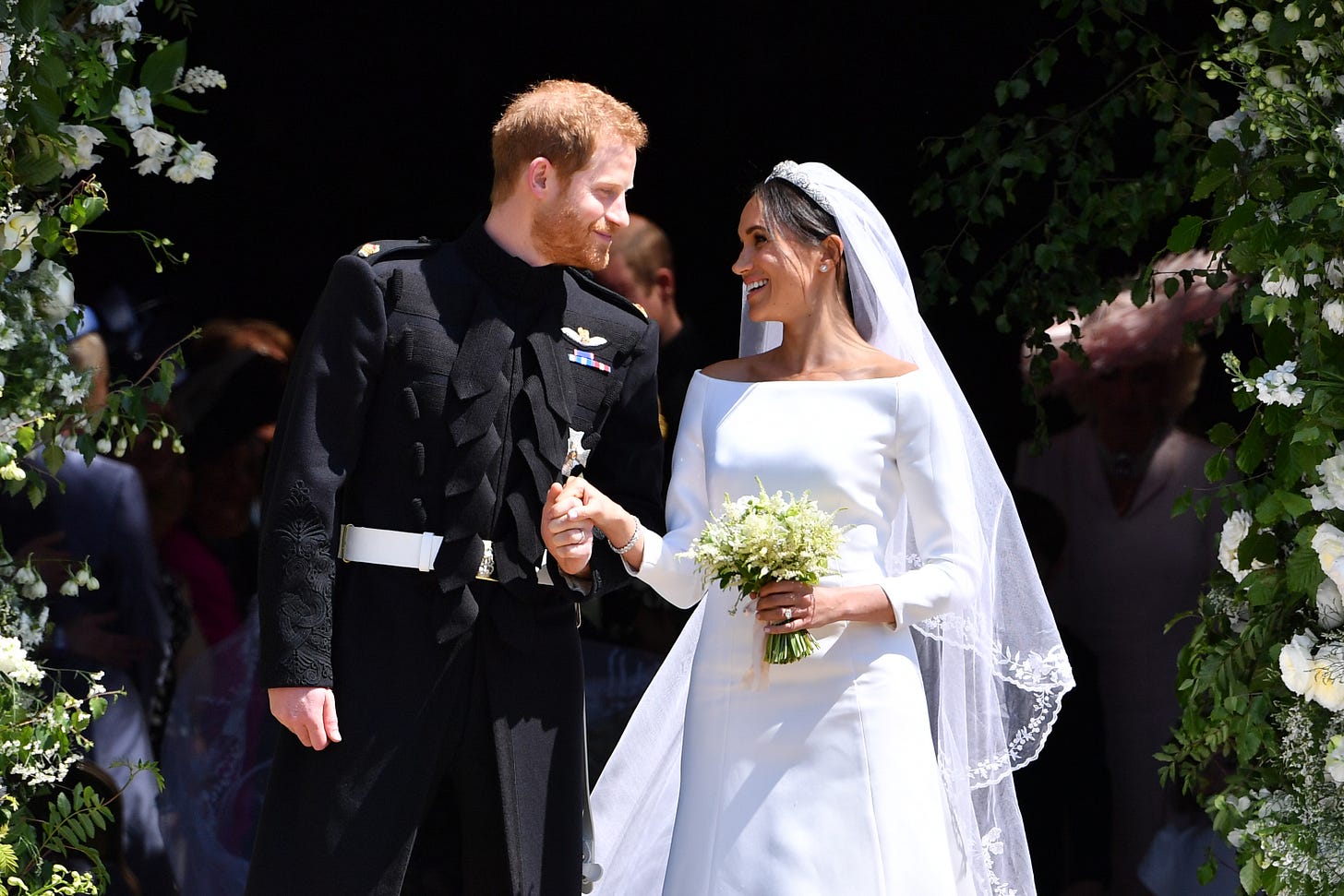 prince harry and meghan markle in a wedding dress both looking at each other fondly