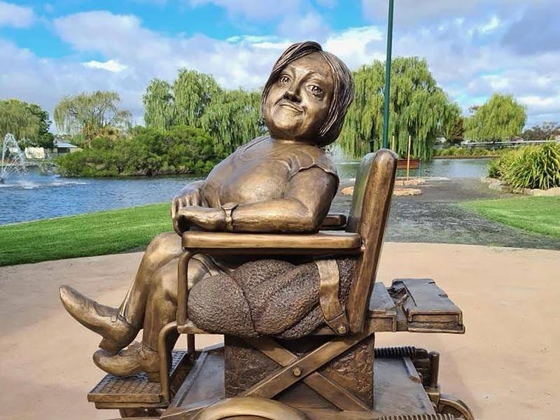 A bronze statue of a small white woman sitting in a powerchair.