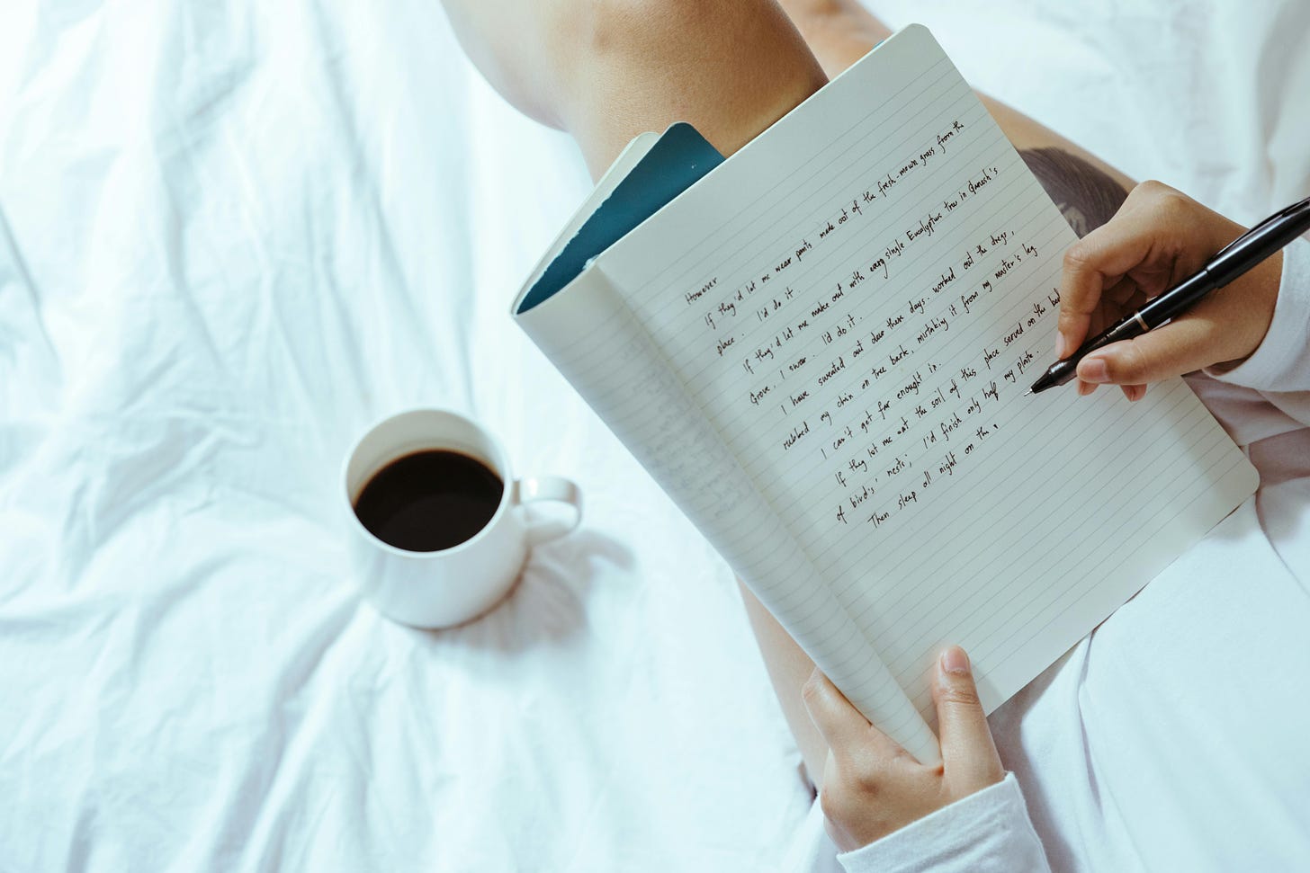 Woman with coffee writing in notebook on bed
