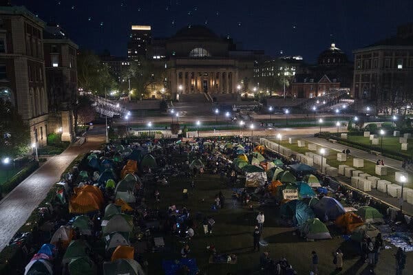 A photo taken at night shows the Columbia campus with protesters and tents.