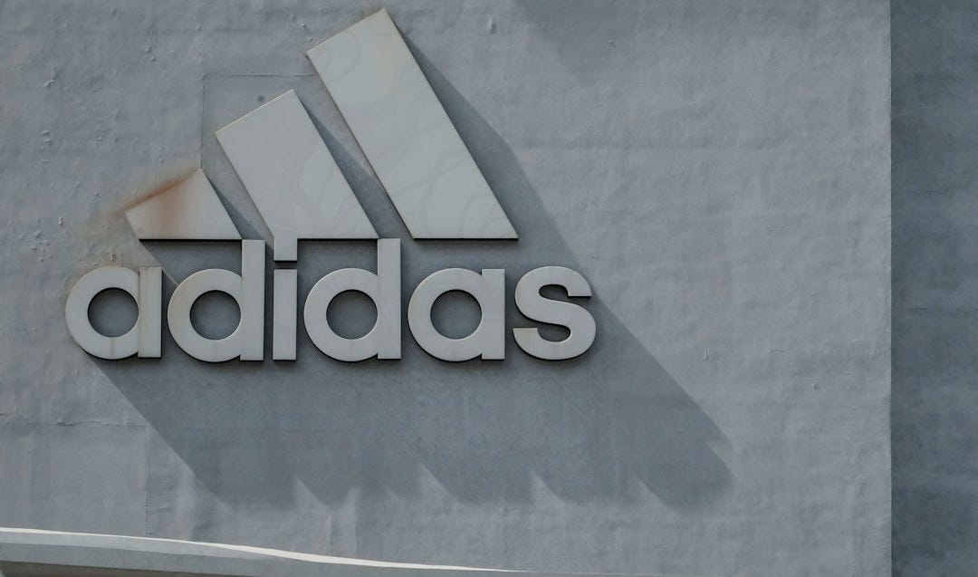 man standing in front of boy leaning on adidas building wall