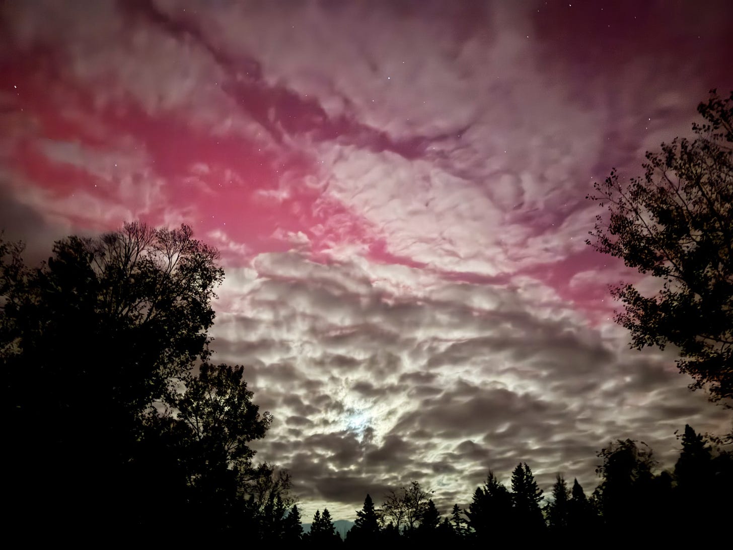 Faint rosy aurora is visible behind a light blanket of clouds.