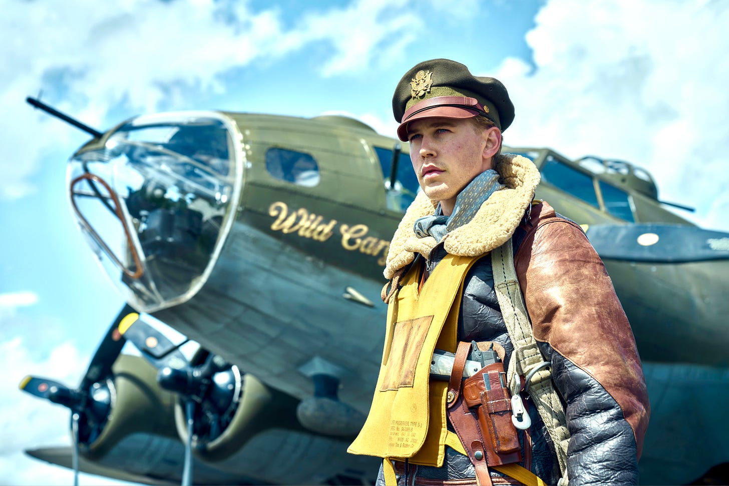 A pilot in a flight suit stands next to a WWII-era bomber