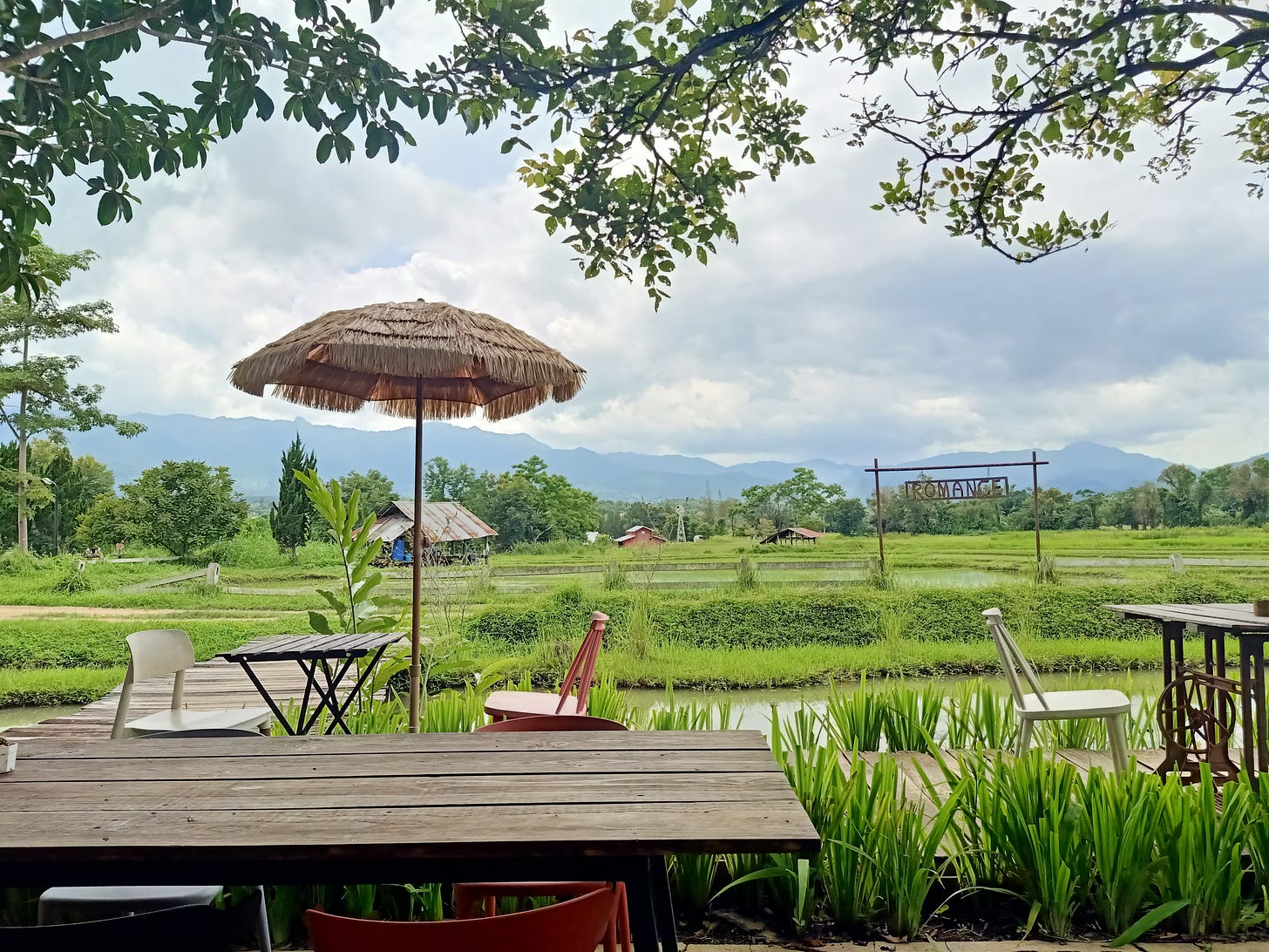 a view of the mountains and fields from a local café with a sign that says "romance" in the distance.