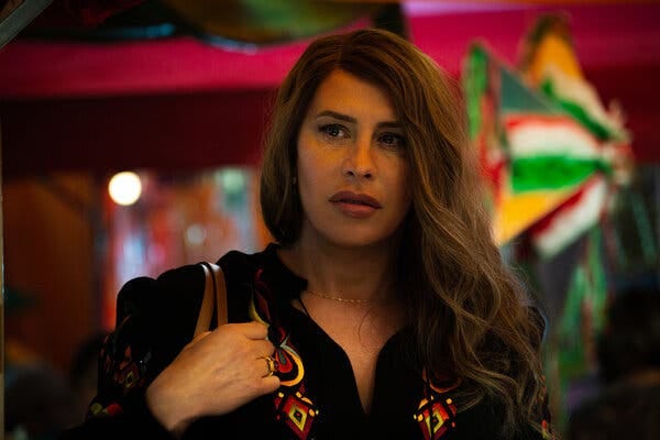 In an indoor scene set against a darkly colorful background, a woman with long hair looks concerned. 