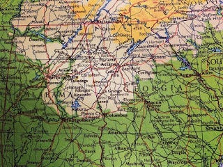 An old atlas shows a map of Alabama and Georgia. The colours are yellow, beige and green.