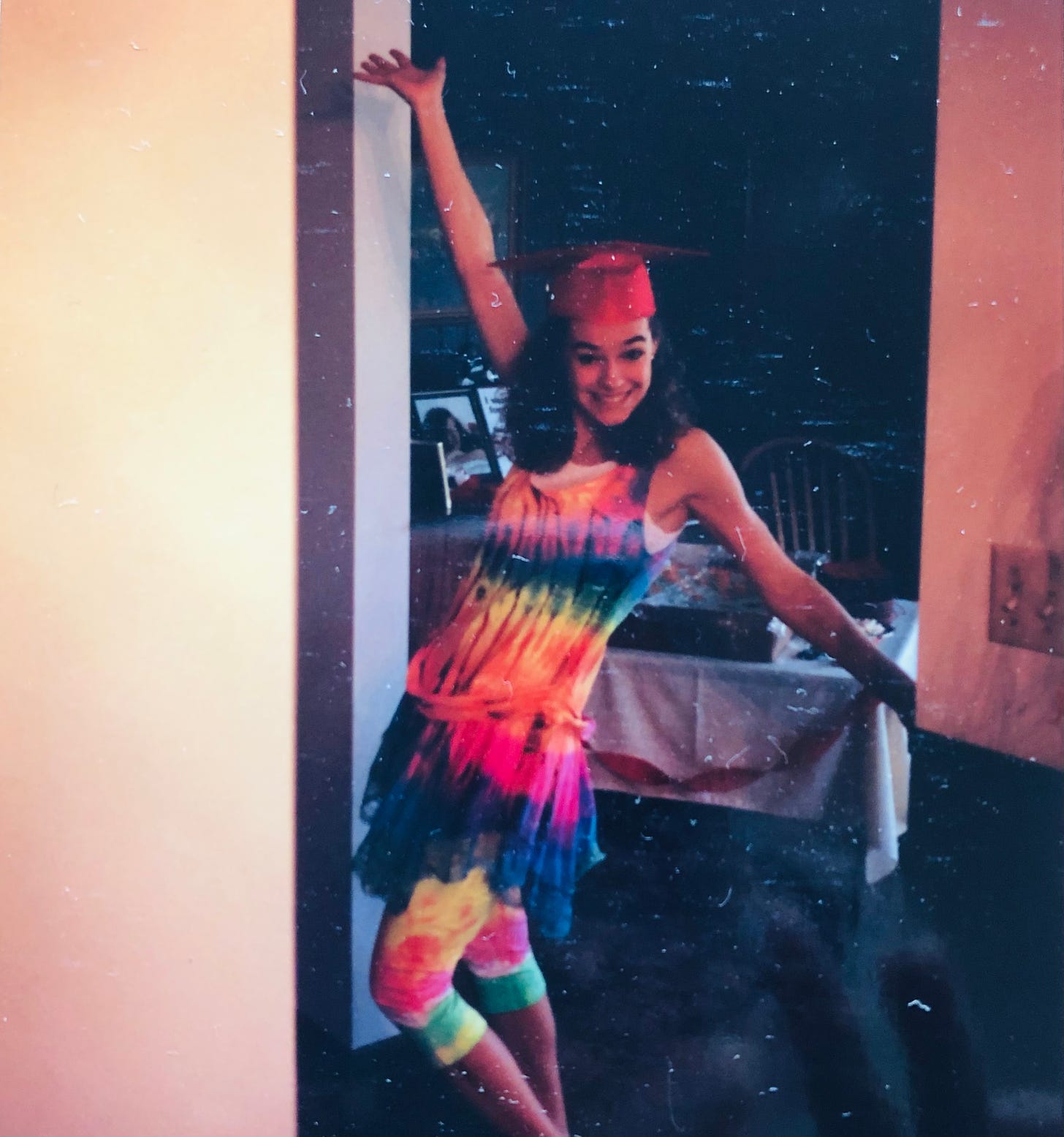 The author in a "tah-dah" pose, wearing a rainbow tie-dyed sundress and leggings beneath her high school graduation cap