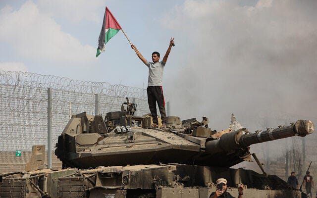 A Palestinian stands on a burning tank in the city of Khan Younis in the southern Gaza Strip after some 3,000 Hamas terrorists destroyed the border fence and entered Israel. October 7, 2023. (Yousef Mohammed/Flash90)