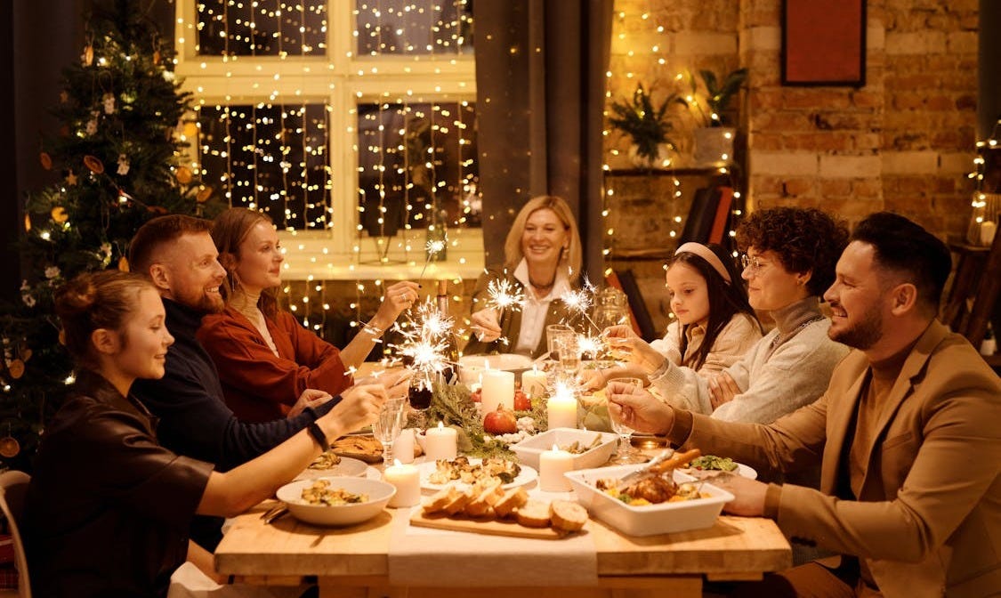 Free Family celebrating Christmas with dinner and sparklers, creating joyful holiday atmosphere indoors. Stock Photo