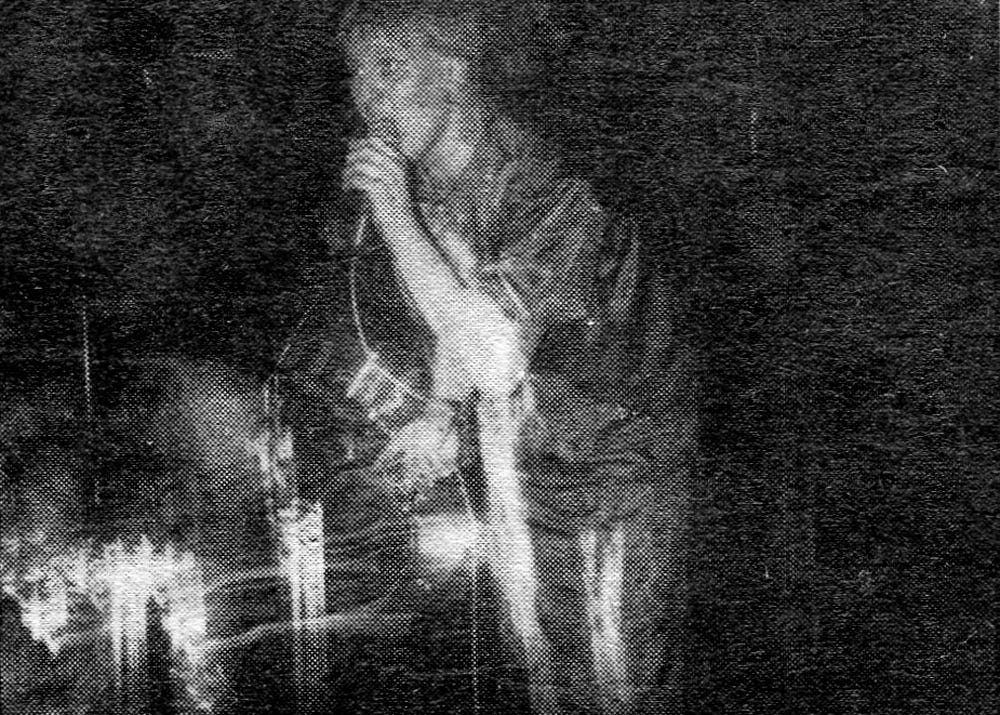 Blurry black and white photo of a person singing into a microphone.