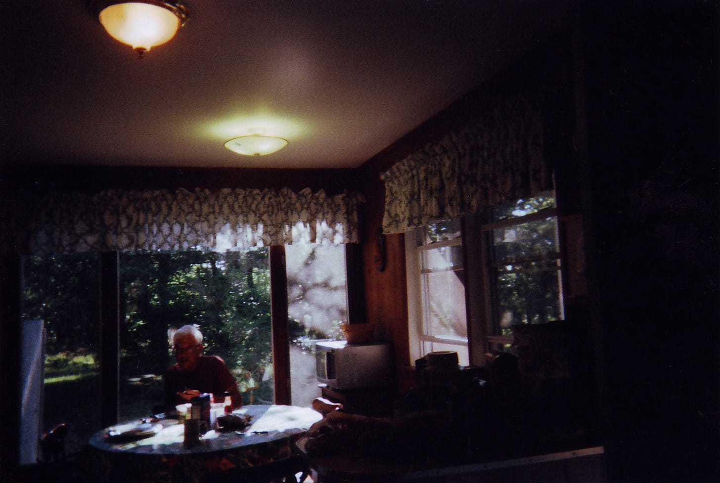 Underexposed photo I took with a disposable camera of my dad sitting at a kitchen table in our Cape rental (luddite teen vibes)