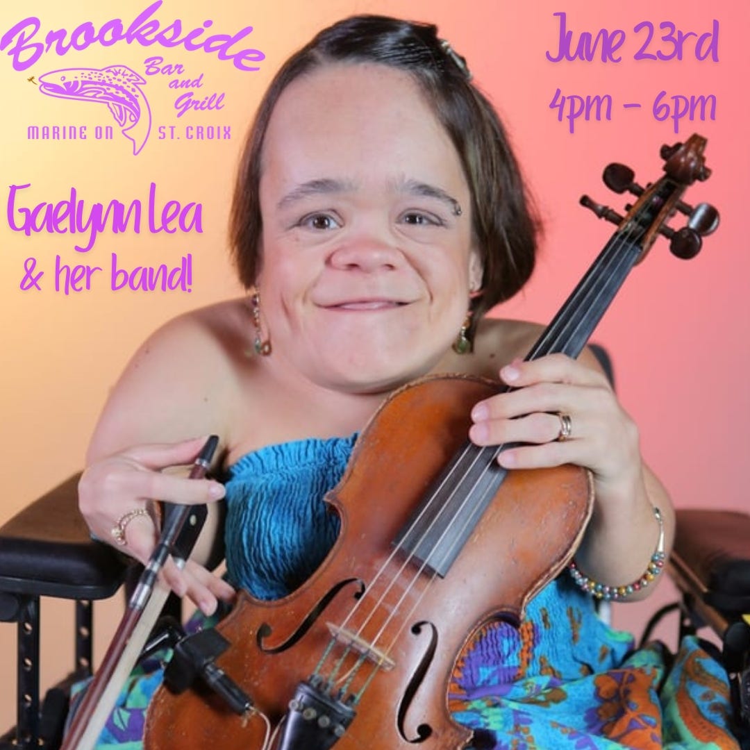 a poster announcing Gaelynn's event at Brookside Bar and Grill. With a background of orange and yellow, Gaelynn smiles as sits in her electrical chair holding her violin and bow. She is wearing a blue dress with flowers of orange and purple. To her left reads Brookside Bar and Grill Marine on St. Croix, Gaelynn Lea, and her band! To her right reads: June 23: 4 PM – 6 PM.