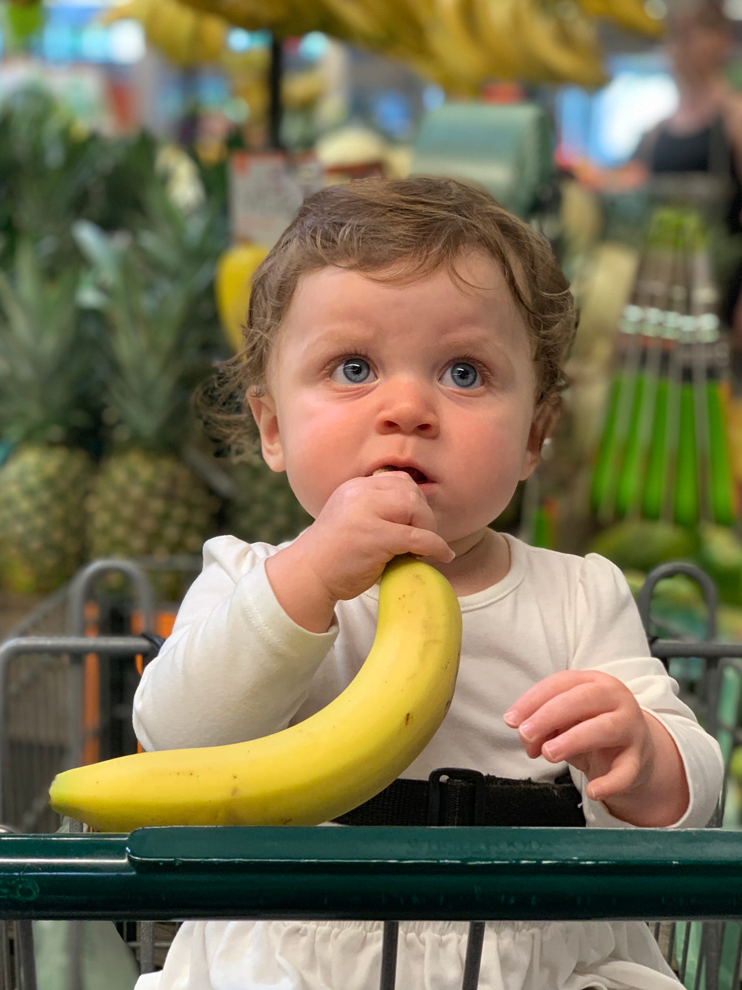 Baby with banana sitting in a shopping cart at a supermarket