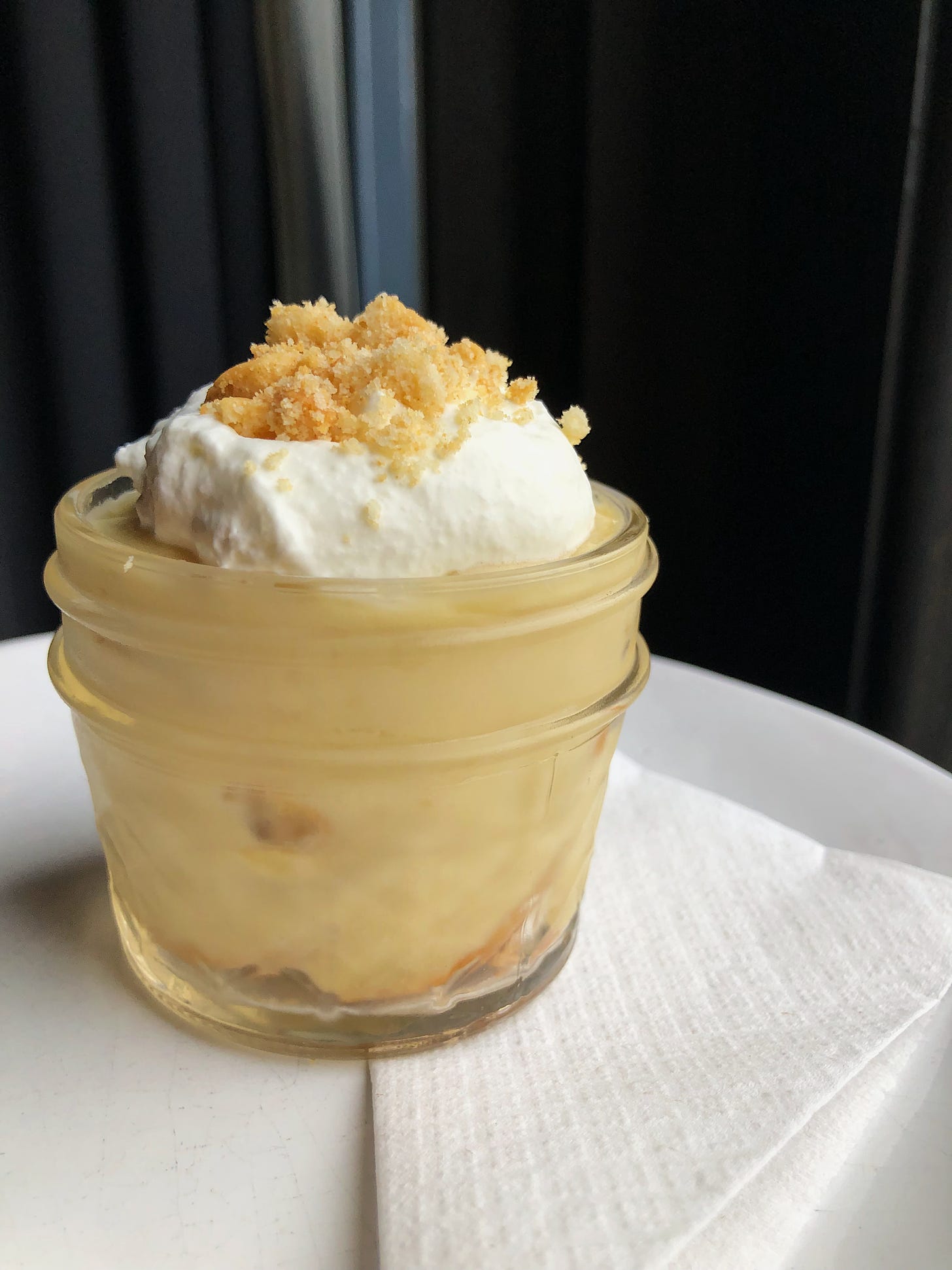 a cup of butterscotch banana pudding with whipped cream and nilla wafer crumbs