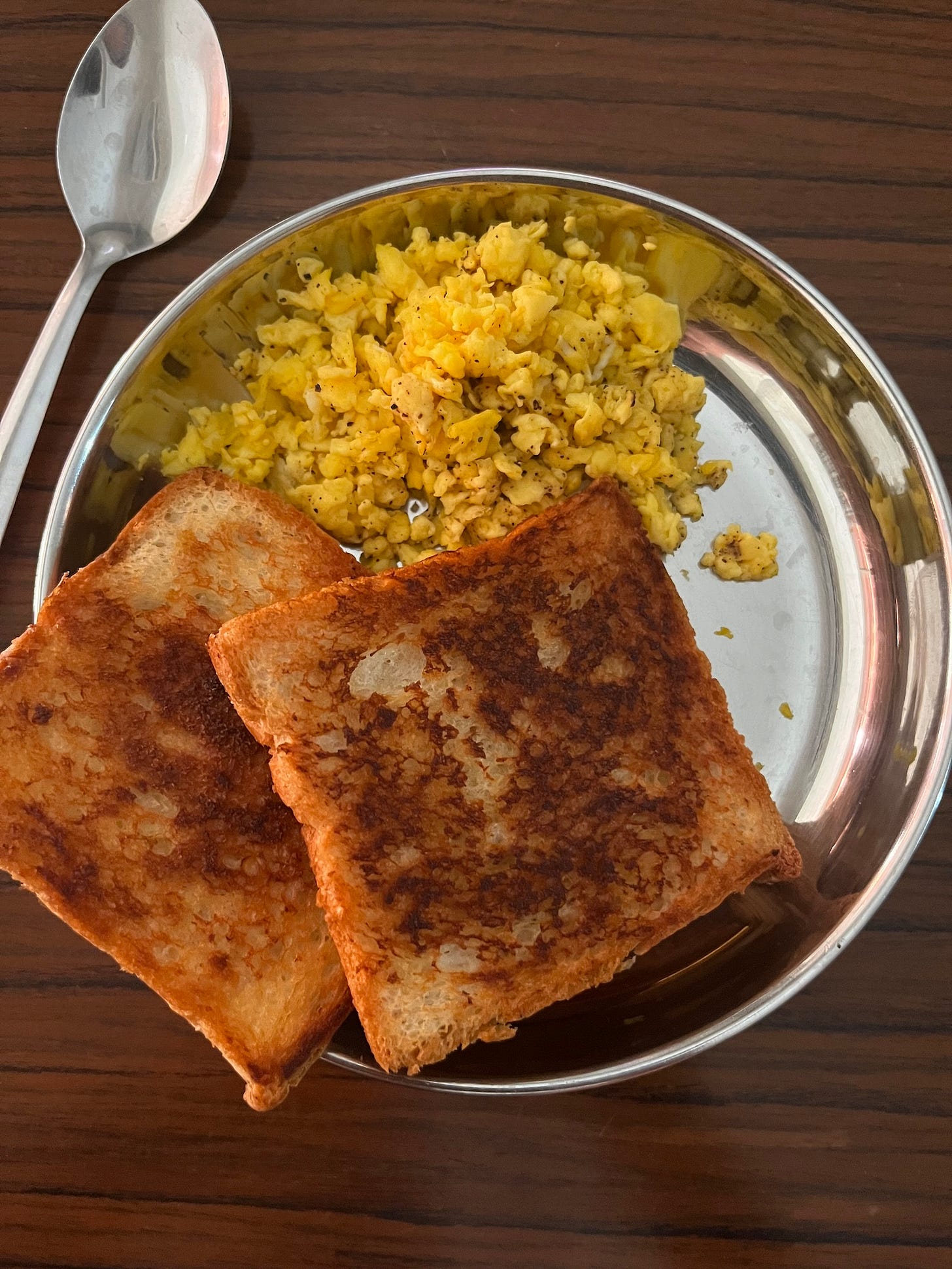 a plate of fried toast and scrambled eggs with a spoon near the plate